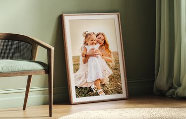Framed photo of woman and child with natural frame and white mat leaned against a green wall next to a modern chair