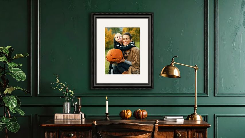 Framed photo of mother and child in a Halloween costume above a desk in a dark green room.