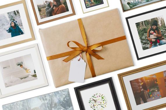 Some photo frames surrounding a gift wrapped in brown paper with a golden ribbon