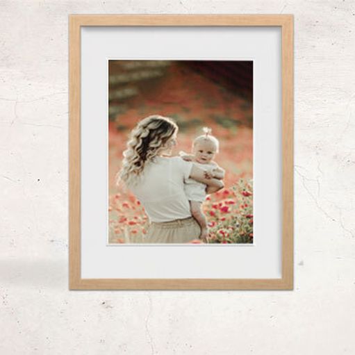 A framed print of a woman holding a baby in a flower grove