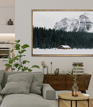 Framed photo of cabin in the snow against a neutral living area with gray couch and plants