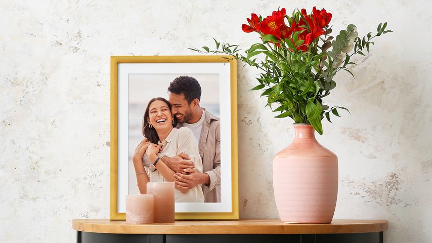 Framed photo of couple in gold frame with white mat next to a vase of flowers