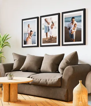 Framed father and child photos in black frames with white mats in a above a brown sofa