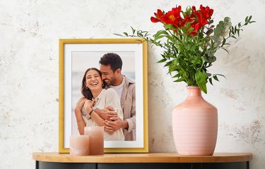 Framed photo of couple in gold frame with white mat next to a vase of flowers