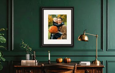 Framed photo of mother and child in a Halloween costume above a desk in a dark green room.