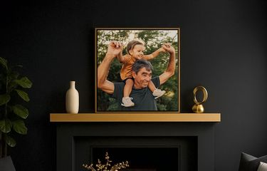 Framed image of grandfather and grandchild above a fireplace in a dark colored room with plant and ceramics