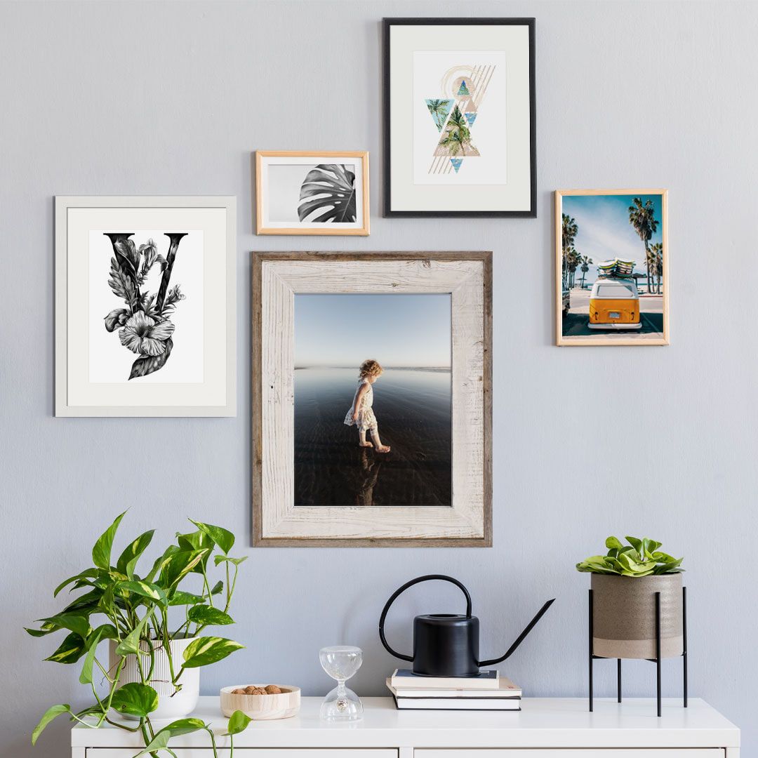 A gallery wall with five framed artworks above a white console table