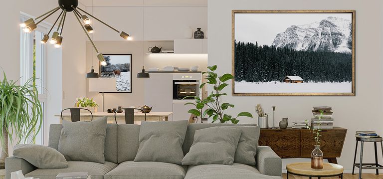 Framed photo of cabin in the snow against a neutral living area with gray couch and plants