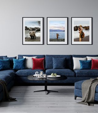 Three framed photos of man and his son walking near water framed in black frames with white mats above a blue sofa with red white and blue accent pillows