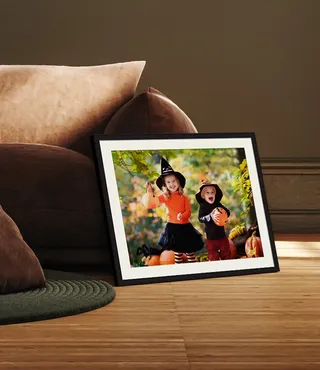 Framed photo of children dressed for Halloween in black frame with white mat next to a tan sofa